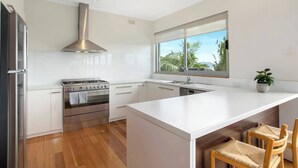 A modern kitchen with a central island, stainless steel appliances, and a large window offering a view of greenery. - Churchill House Riverside Retreat near Long Beach (Sandy Bay)