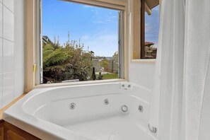 A bathroom with a large bathtub, a window, and a view of a garden.