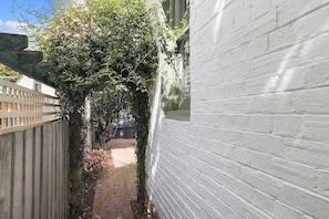 A narrow brick pathway flanked by a white brick wall and a wooden fence.