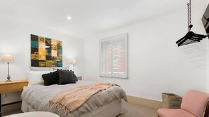 Een slaapkamer met een bed, nachtkastjes, een stoel, een raam met zonwering en een hanglamp.