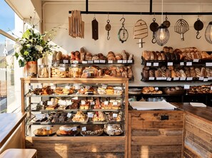 A bakery with shelves of bread and pastries, a display case with baked goods, and hanging kitchen utensils. - Toris Cottage Stroll to Vibrant Salamanca (Battery Point)