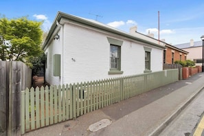 A single-story house with a white exterior and green trim, number 36, with a picket fence and a paved driveway.