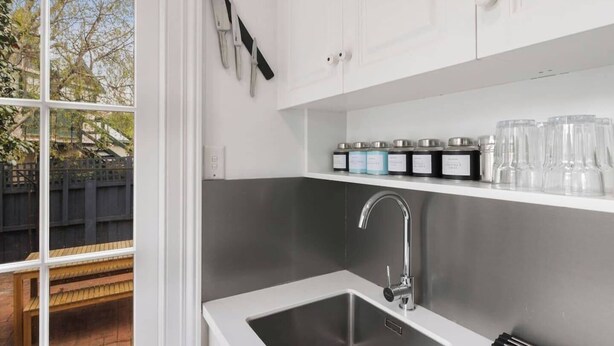 Een moderne keuken met een roestvrijstalen spoelbak, witte kastjes en een raam met uitzicht op een achtertuin.