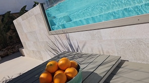 A poolside area with a stone wall and a table with a bowl of oranges.