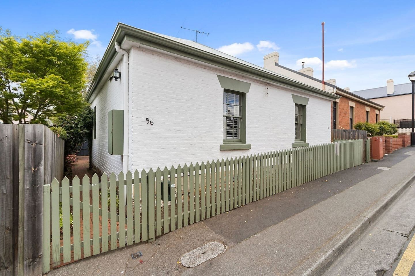 A single-story house with a white exterior, a green picket fence, and a number '36' on the wall.