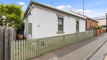 A single-story house with a white exterior, a green picket fence, and a number '36' on the wall.