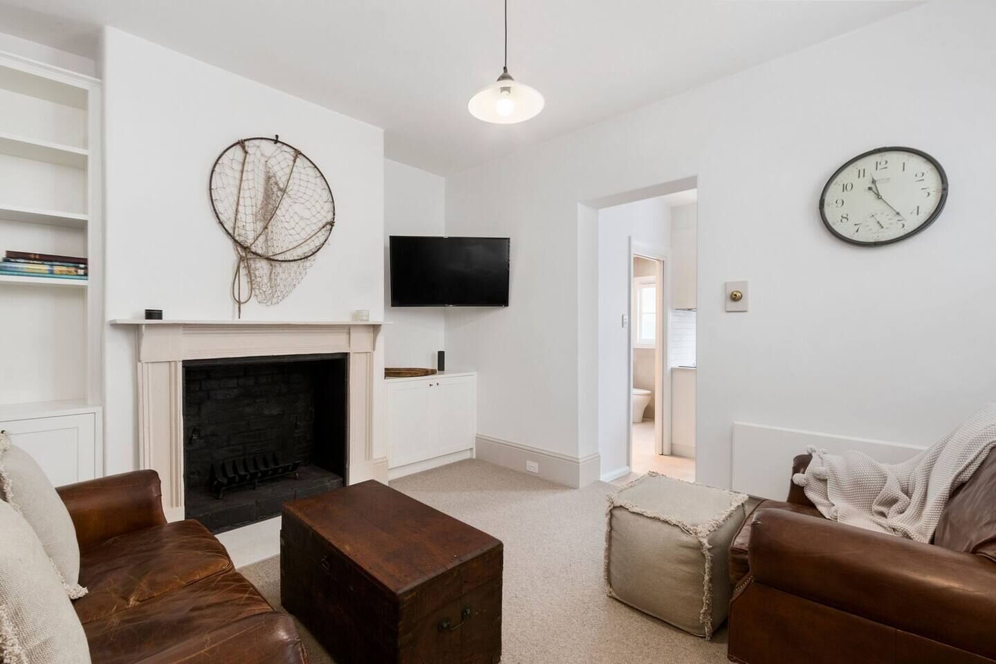 A living room with a fireplace, leather sofas, a coffee table, a wall-mounted TV, and a clock.