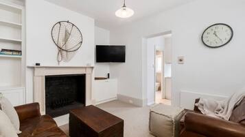 A living room with a fireplace, leather sofas, a coffee table, a wall-mounted TV, and a clock.