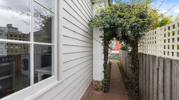 A narrow brick pathway leading to a wooden fence, with a white building on one side and a red building in the background.