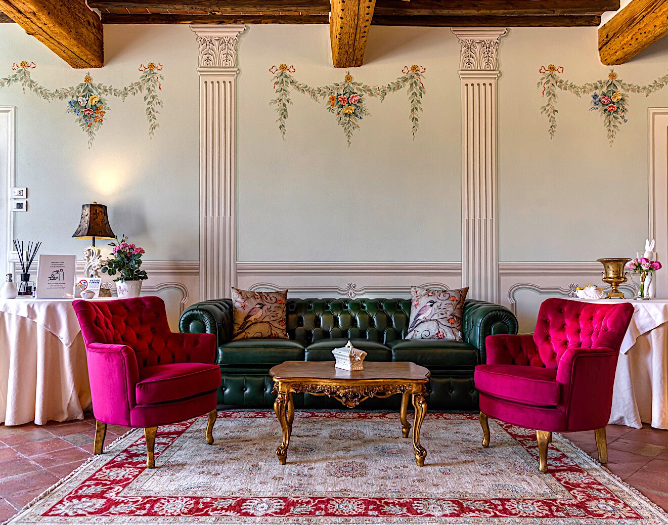 Una habitación con un sofá verde, dos sillones rojos, una mesa dorada y una alfombra estampada.