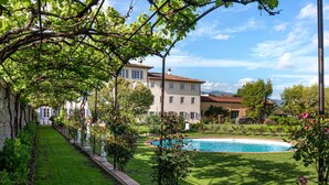 A poolside view with a well-maintained lawn, a stone bench, and a large building with a tiled roof.