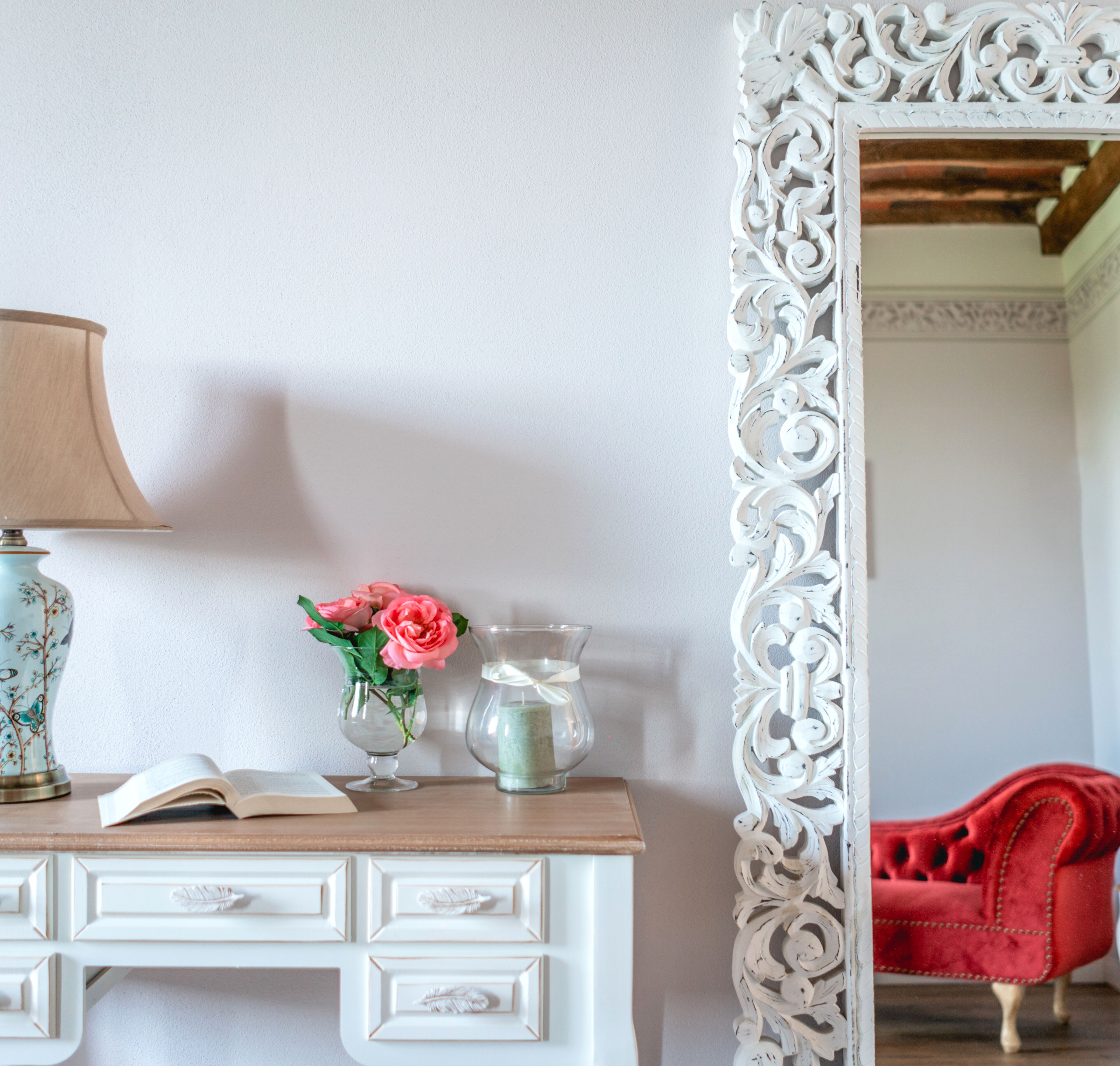 Ein weißer Kommode mit Schubladen, eine Lampe, eine Vase mit rosa Blumen und eine Kerze.