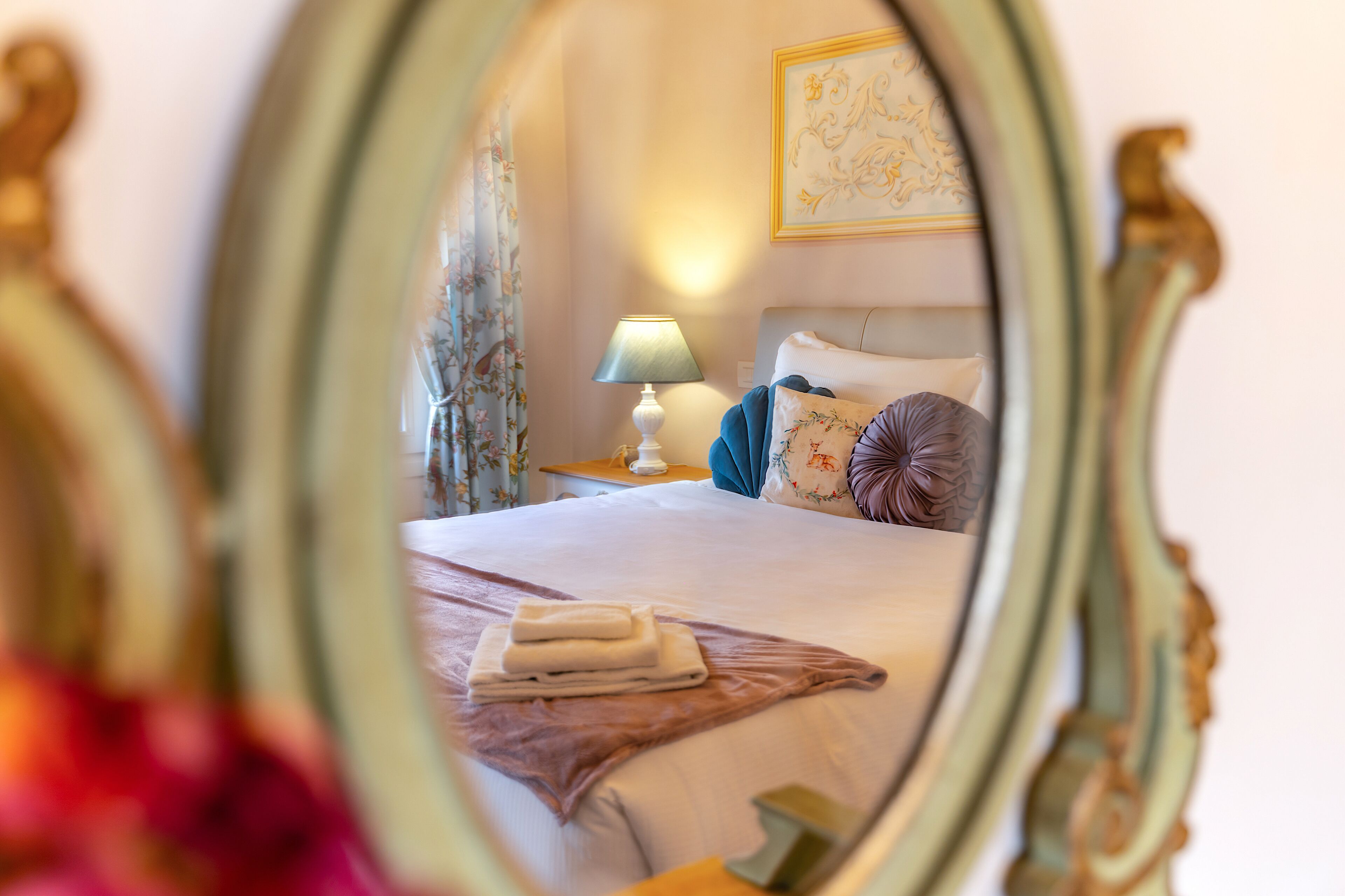 Een slaapkamer met een netjes opgemaakt bed, een bedlampje en een bloemverfijning aan de muur.