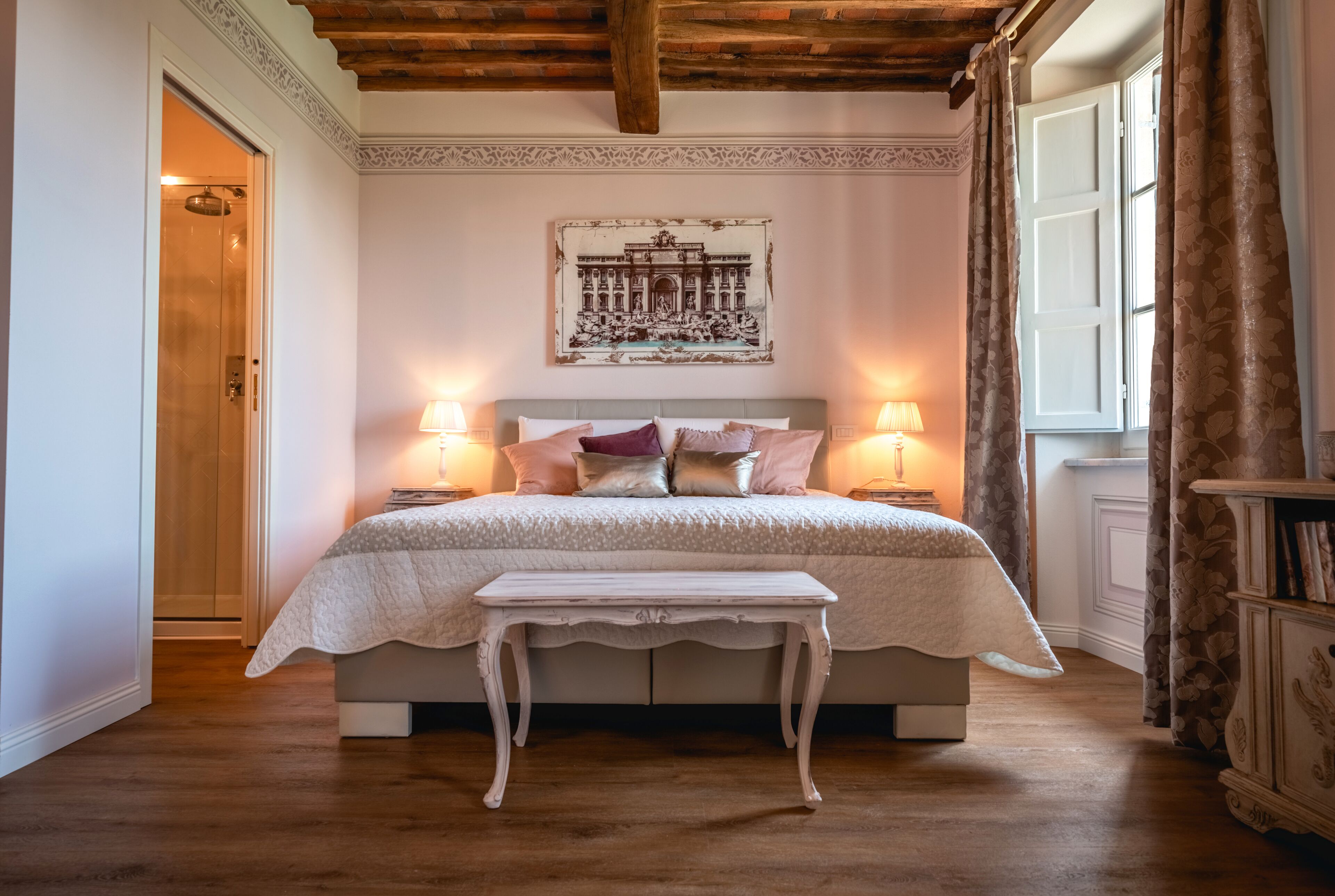 Een slaapkamer met een bed, nachtlampjes, een bankje, een decoratief object aan de muur, en een raam met gordijnen.