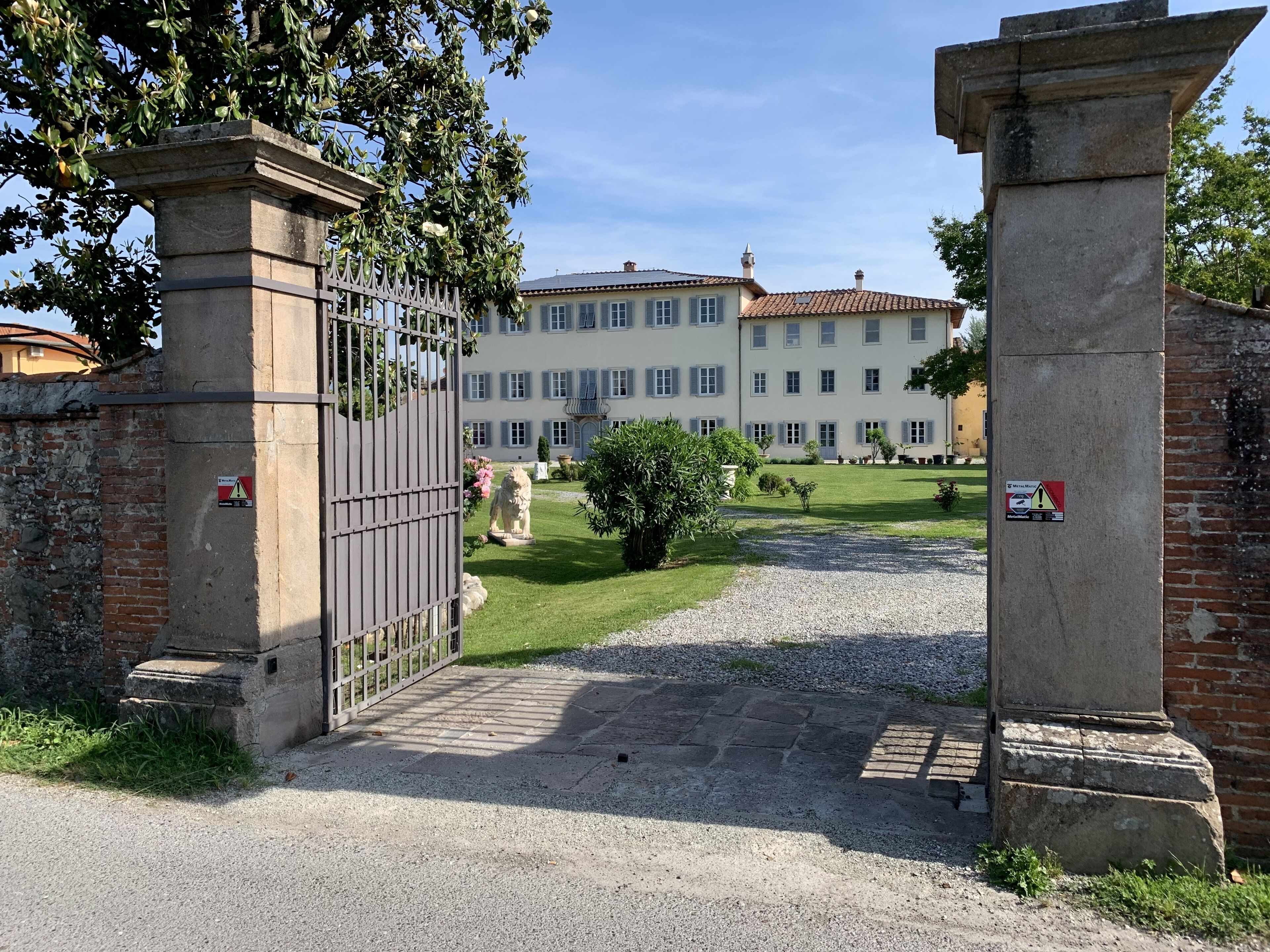 A gated entrance to a building with a paved driveway leading to a grassy area with a statue.