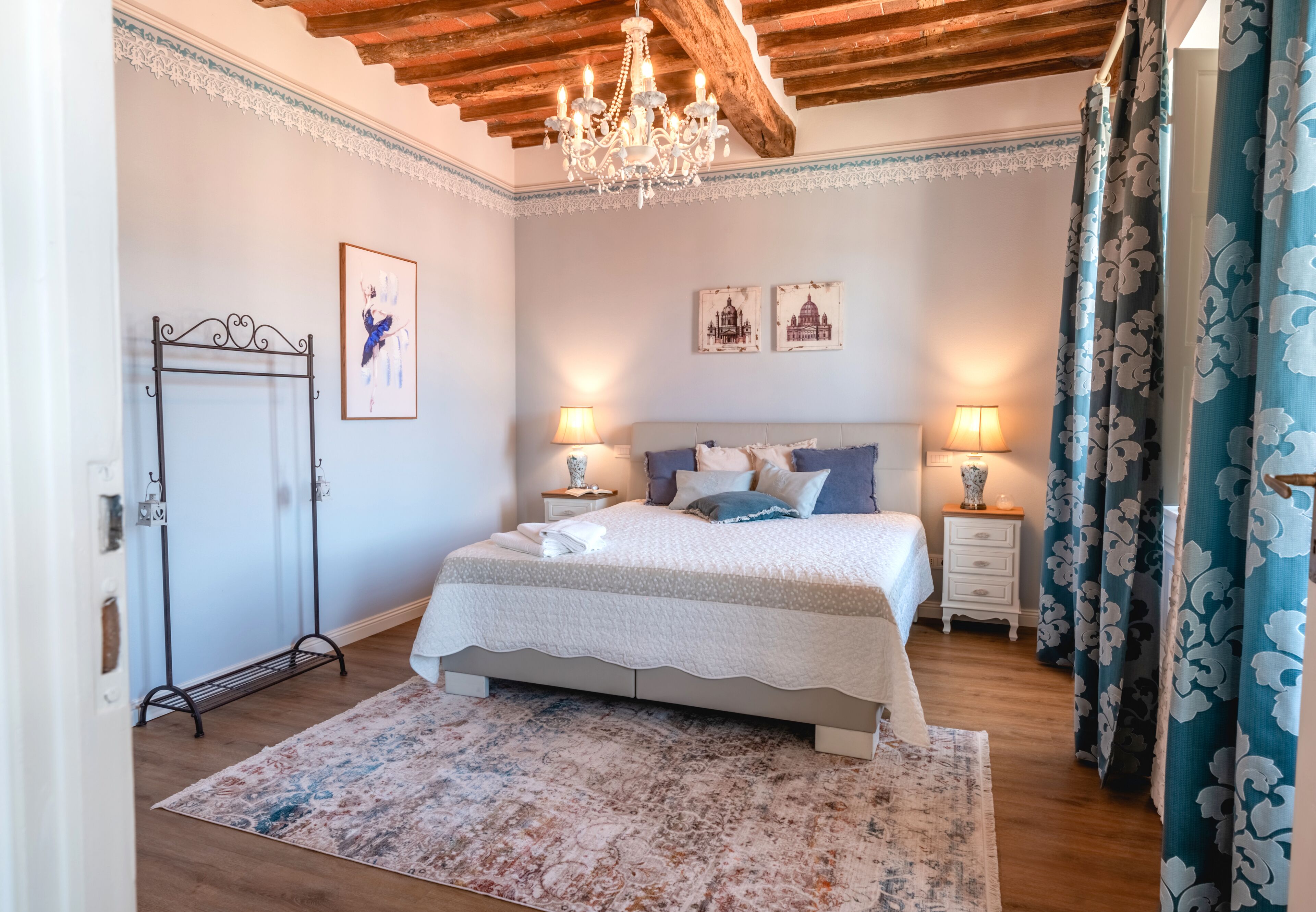 A bedroom with a bed, nightstands, a chandelier, a wardrobe, and a floral curtain.