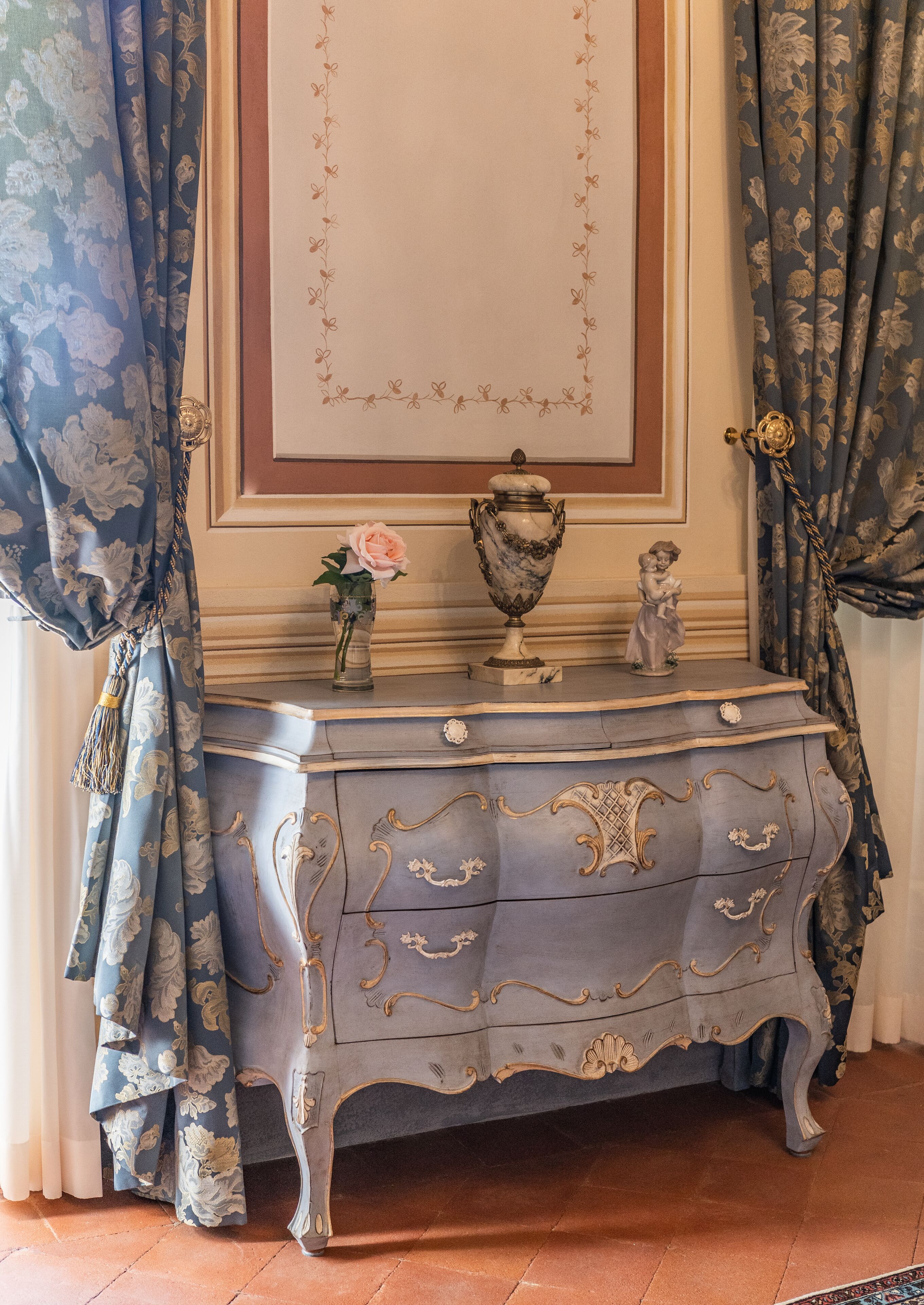 Un comò in stile vintage con elaborate decorazioni intagliate e un vaso con un fiore rosa.