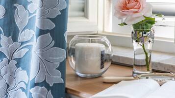 A room with a window, a candle, a vase with a rose, and an open book on a wooden table.
