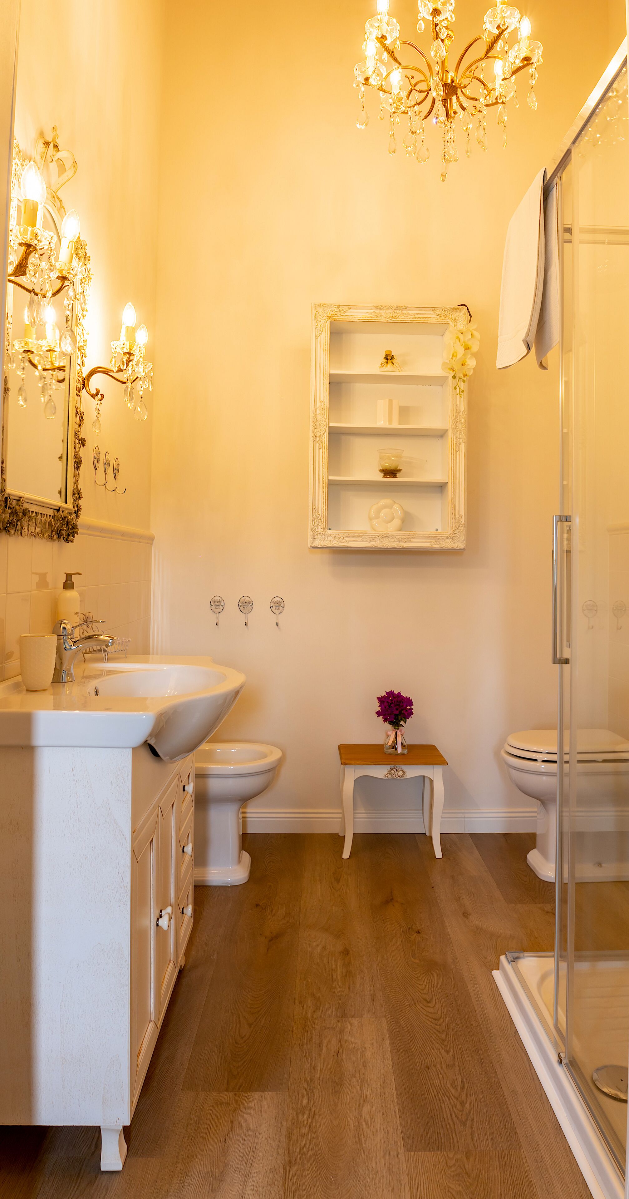 A bathroom with a white sink, two toilets, a shower, a vanity with drawers, a mirror, and a chandelier.