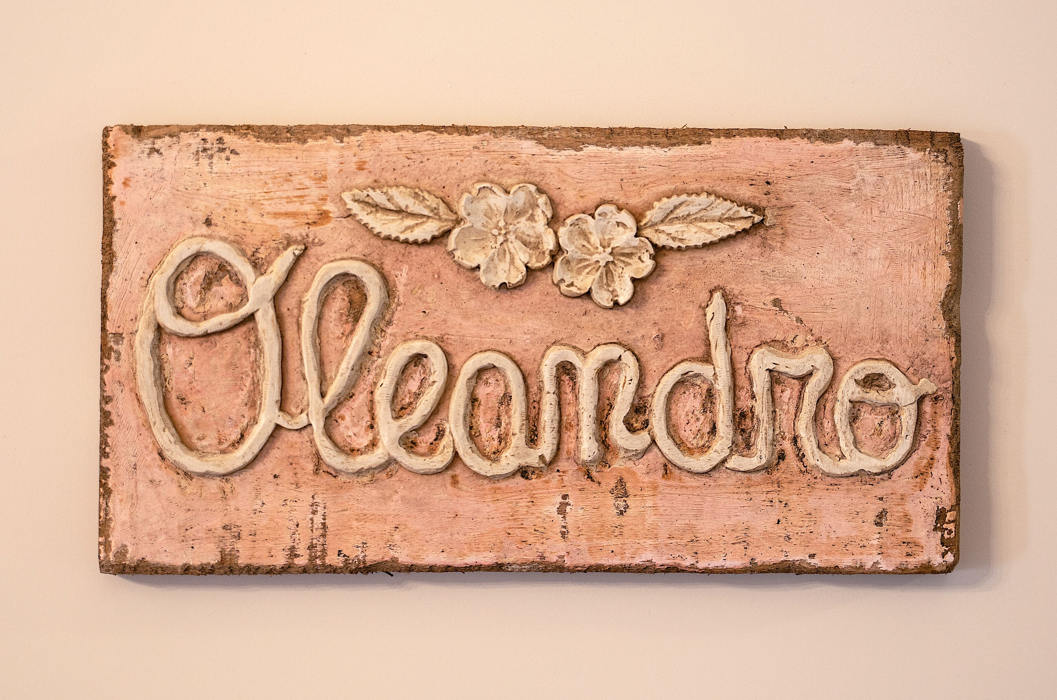 Un letrero de madera rústico con la palabra 'Cleandro' y detalles florales decorativos.