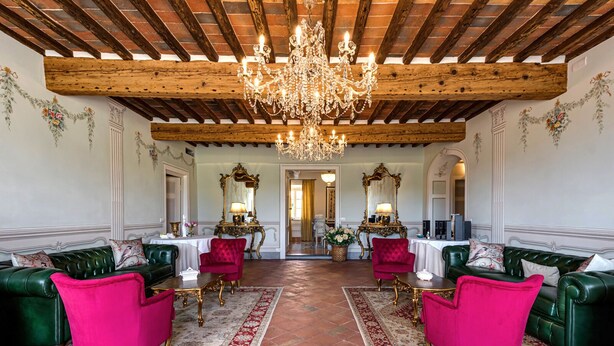 A room with a wooden ceiling, green upholstered sofas, a chandelier, and two ornate mirrors.