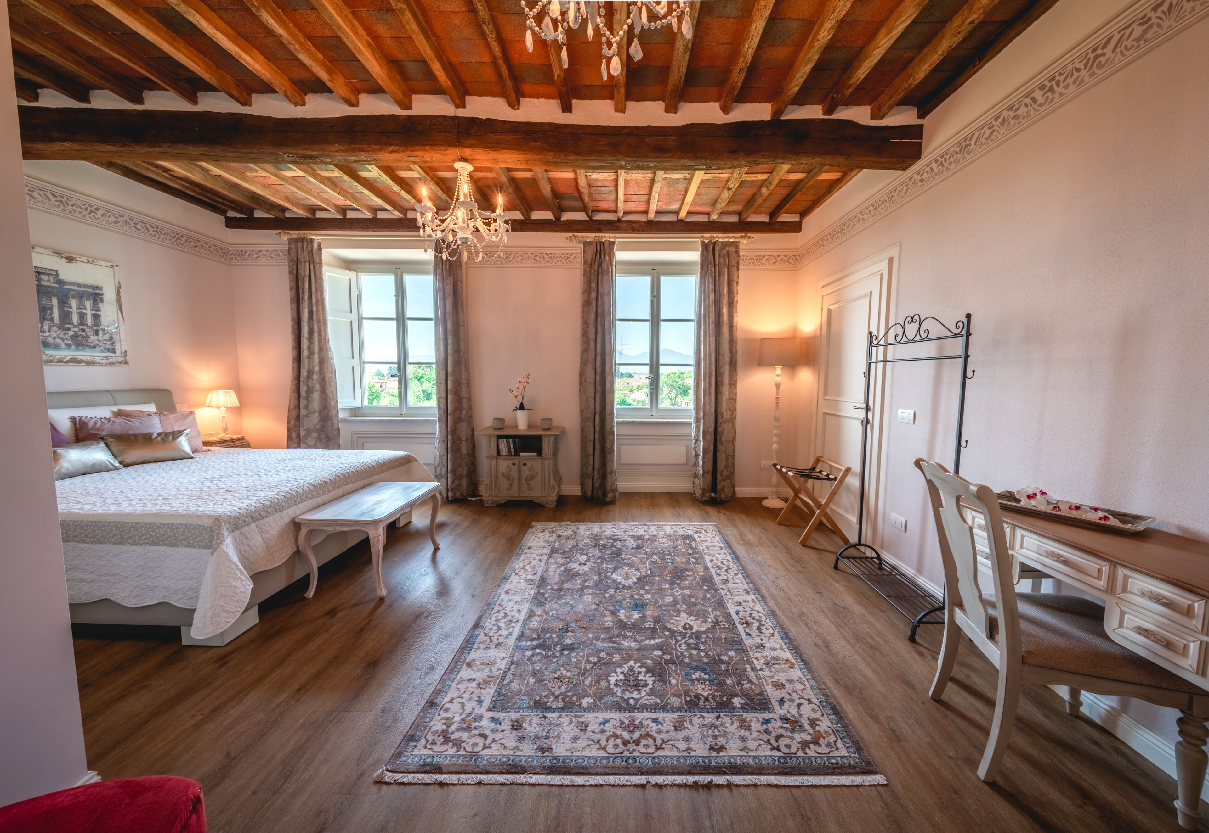 Quarto com teto de madeira, uma cama grande, escrivaninha e vista para o exterior através de duas janelas.