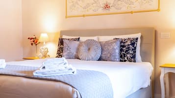 Een keurig opgemaakt bed met een grijze hoofdbord, een bloemrijk kunstwerk erboven en een nachtkastje met een lamp en een bloemenvaas.