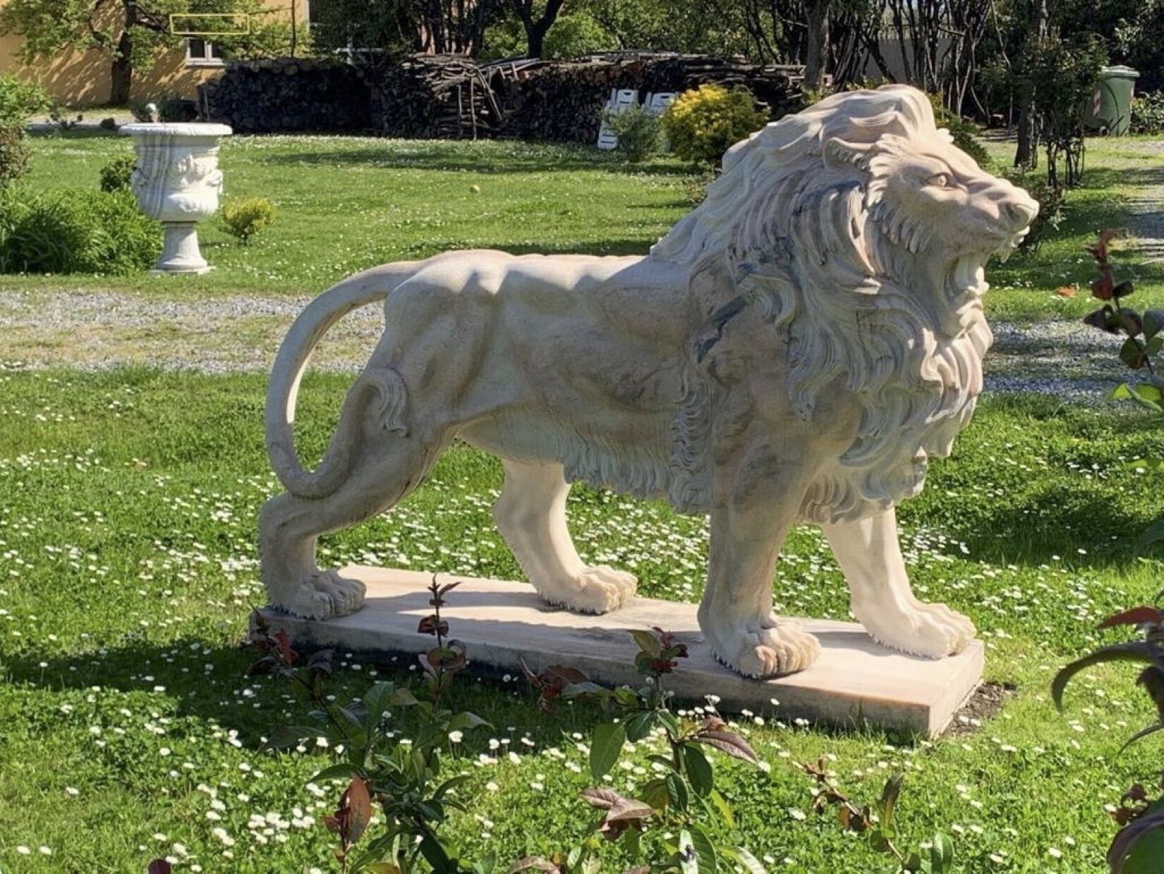 Eine Steinstatue eines Löwen in einem Garten mit Gras und Blumen.