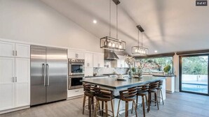 A modern kitchen with stainless steel appliances, a large island with bar stools, and pendant lighting. - Skyline: 5 bed/6 bath, amazing views, tennis & basketball courts, pool, hot tub (Catalina Foothills)