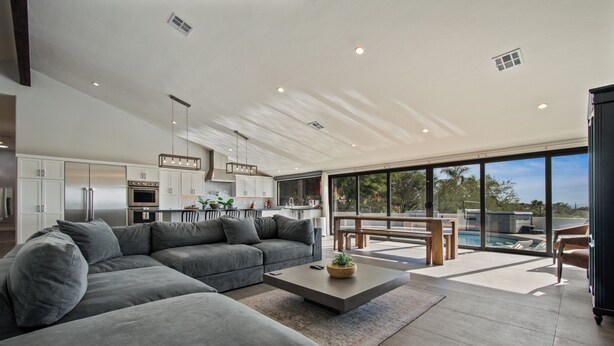 A modern living space with a large gray sectional sofa, a minimalist coffee table, and a dining area with a bench. The kitchen features white cabinets and stainless steel appliances. - Skyline: 5 bed/6 bath, amazing views, tennis & basketball courts, pool, hot tub (Catalina Foothills)