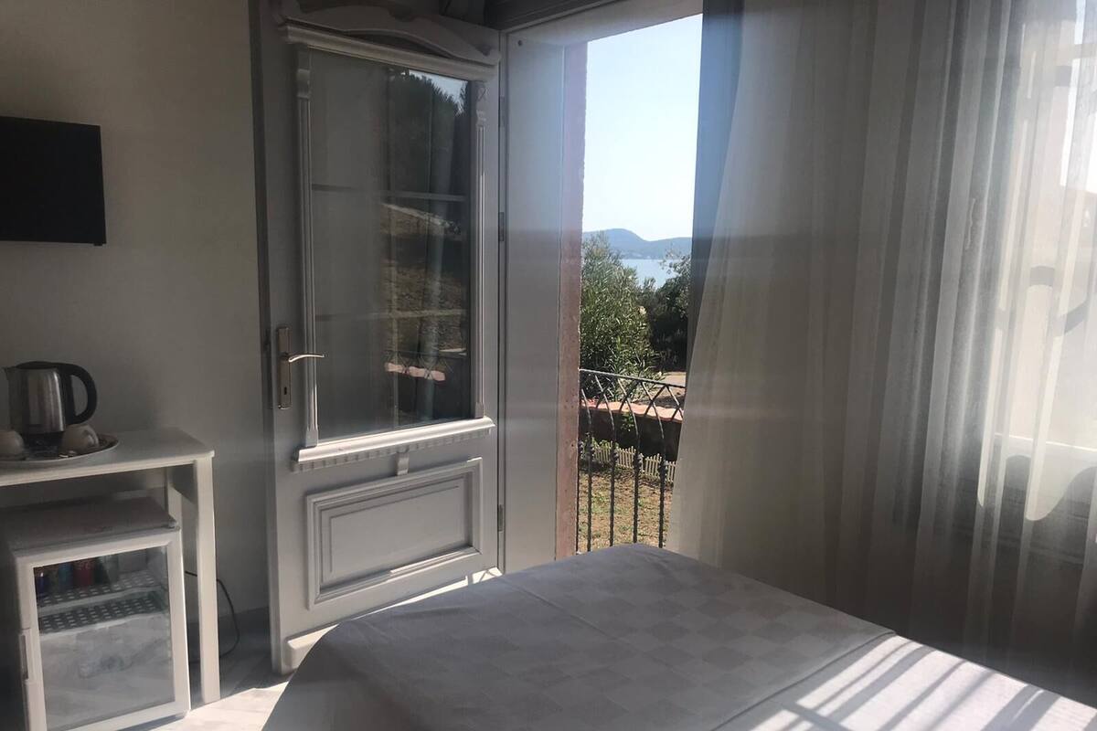 Un dormitorio con una cama, una mesita con hervidor y una ventana con vistas a un jardín y colinas.
