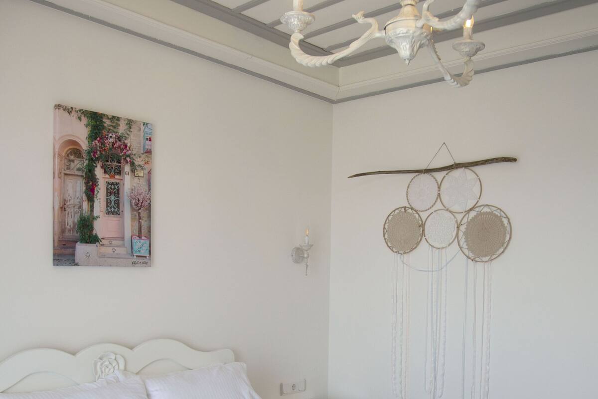 Un dormitorio con una cama, una mesita de noche, un atrapasueños colgado en la pared y un cuadro.
