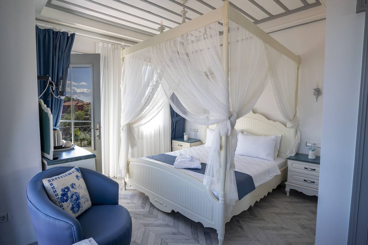 Un dormitorio con cama con dosel, una silla con cojín floral y una ventana con cortinas.