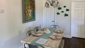Een eetkamer met een houten tafel voor vier personen, een kroonluchter en een kleurrijk schilderij aan de muur.