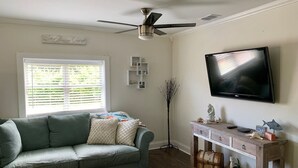 Een woonkamer met een grijze bank, een houten console en een televisie, plus een plafondventilator.