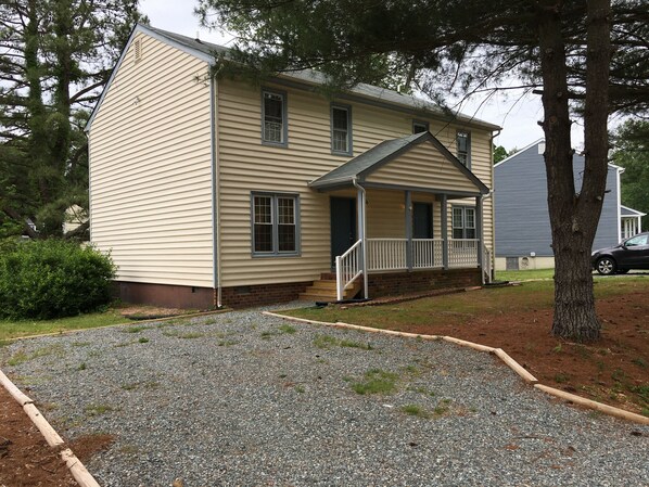 A two-story house with a front porch, a small front yard with gravel, and a tree in the foreground. - Duplex Apt (Sunshine Suite) (Richmond)