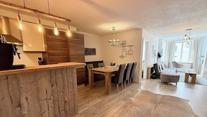 Une cuisine moderne avec des meubles en bois, un coin repas avec une table et des chaises en bois, et un espace de vie comprenant un canapé et une table basse.
