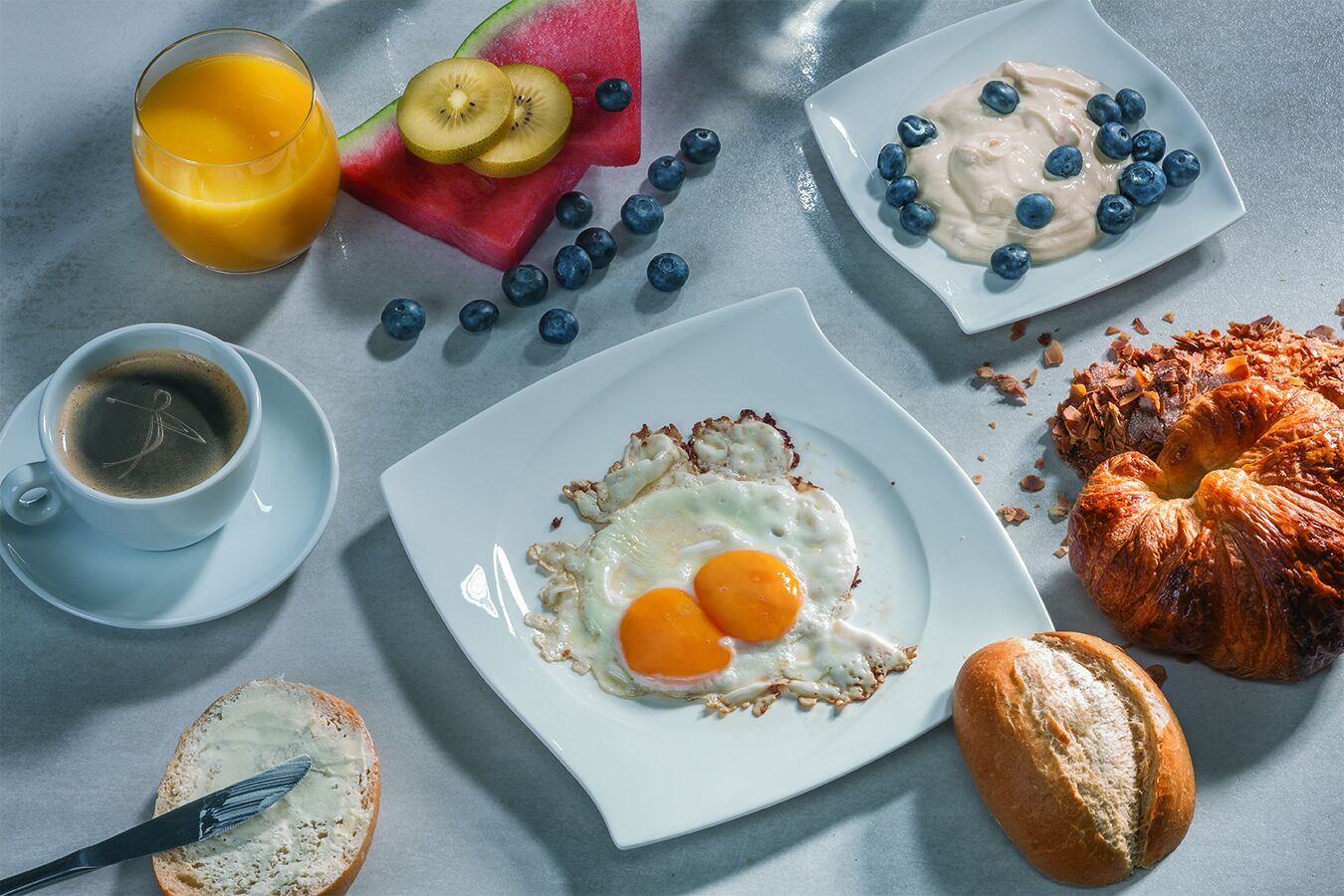 A breakfast setting with a plate of eggs, toast, croissant, and fruit.