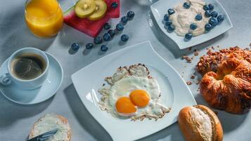 A breakfast setting with a plate of eggs, toast, croissant, and fruit.