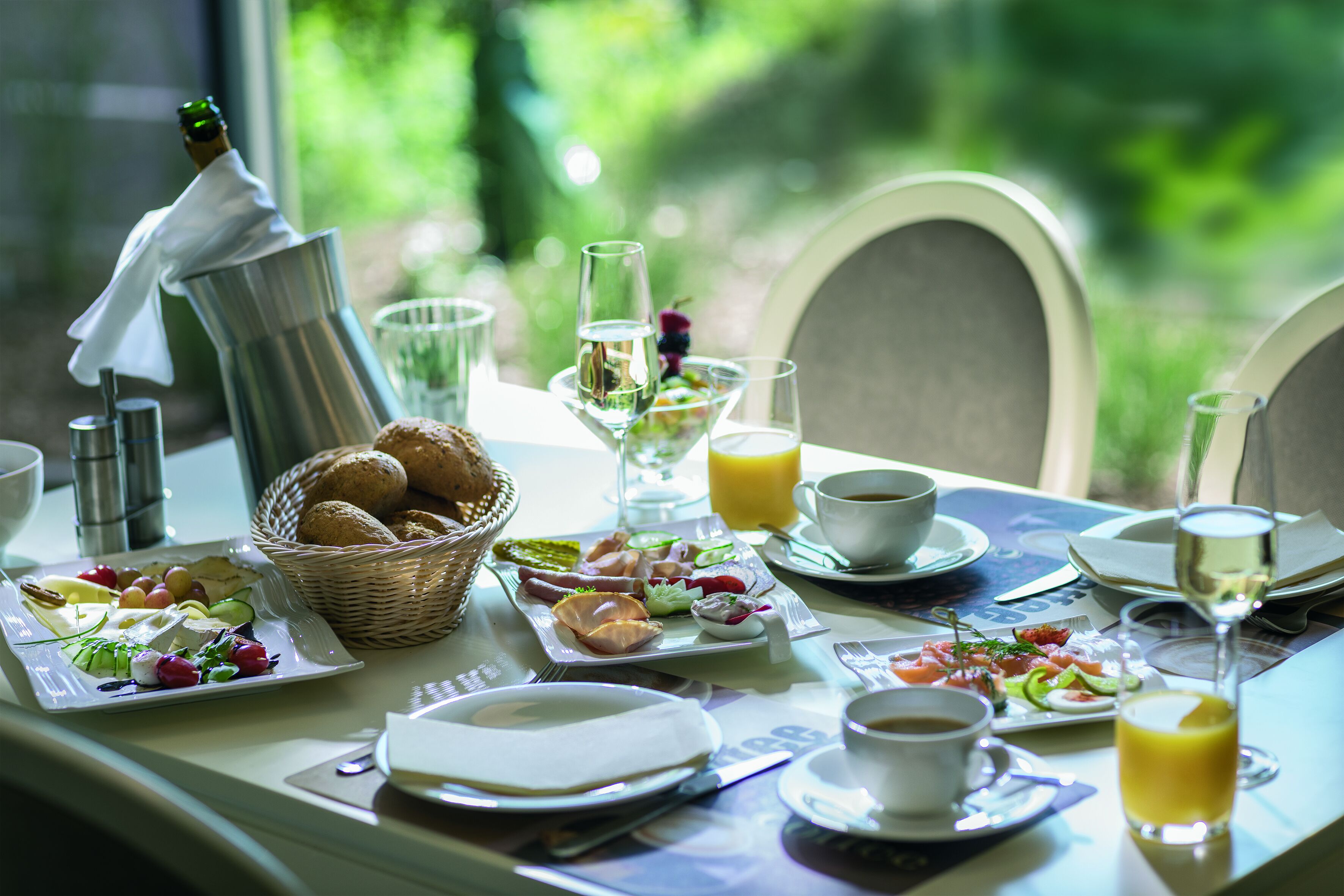Una mesa de desayuno servida con diversos platos, incluyendo huevos, tostadas y fruta, junto con una botella de champán y copas.