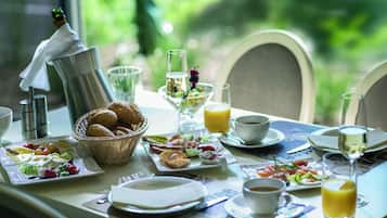 Una mesa de desayuno servida con diversos platos, incluyendo huevos, tostadas y fruta, junto con una botella de champán y copas.