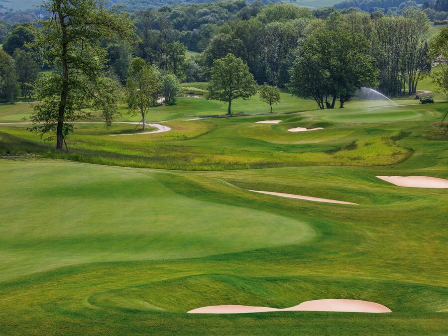 Un campo de golf con bunkers de arena, árboles y un sistema de aspersión.