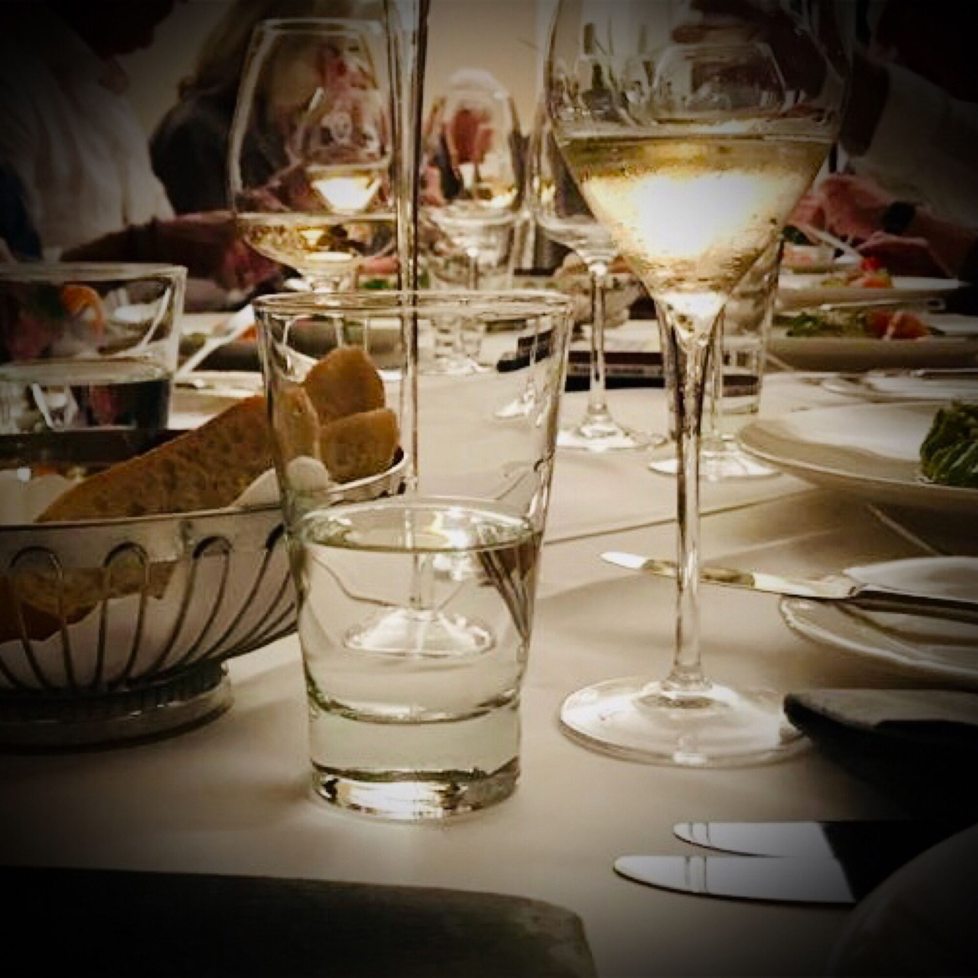 A dining table with multiple wine glasses, a bowl of bread, and plates of food.