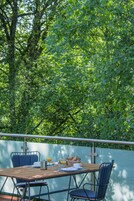 Un espacio para comer al aire libre con una mesa preparada para dos personas, rodeado de abundante vegetación.