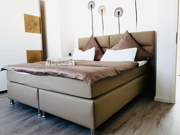 A modern bedroom with a large bed, a wooden headboard, and a decorative wall piece.