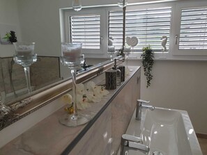 A modern bathroom with a large mirror, a bathtub, and a window with blinds.