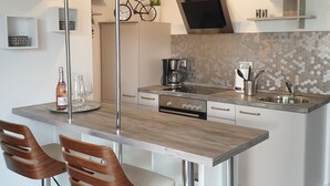 A modern kitchen with a central island, bar stools, a coffee machine, and a microwave.