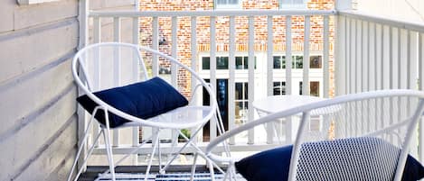 Ein Balkon mit zwei weißen Stühlen und einer blau-weiß gestreiften Decke.