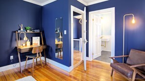 Une pièce comprenant un bureau, une chaise et un fauteuil en cuir marron. Une porte blanche donne accès à une salle de bain équipée d’un lavabo et d’un miroir.