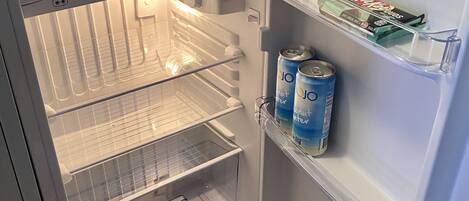 An open refrigerator with a water dispenser, a milk carton, and two cans of soda.